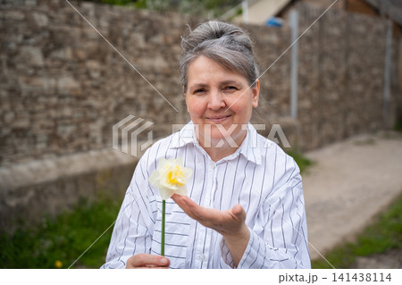 Smiling older woman holding a flower outdoors in a rustic environment. Emotional wellbeing menopause support and nature therapy for healthy aging 141438114