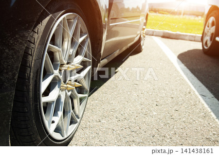 Close-up view of car wheel with custom bullet shaped lug nuts in parking lot under bright sun light, showcasing vehicle personalization and modern automotive style modification 141438161