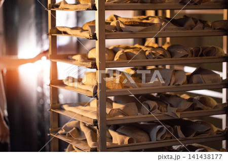 Unbaked bread loaves resting on proofing racks in traditional commercial bakery; manual preparation of artisanal bread for baking process Unbaked bread loaves resting on proofing racks in traditional commercial bakery; manual preparation of artisanal bread for baking process 141438177