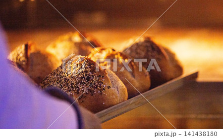 Artisan bread loaves with various seed topping on wooden peel, hand inserting into glowing hot oven, manual bakery production, fresh baked. 141438180