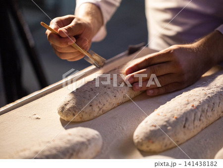 Baker hands preparing artisan bread dough loaves for baking on floured surface manufacturing process fresh bakery product production factory setting Baker hands preparing artisan bread dough loaves for baking on floured surface manufacturing process fresh bakery product production factory setting 141438182