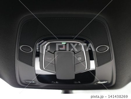 Modern automotive interior overhead console showing control panel with buttons for lights and emergency SOS function, featuring sleek design and a green indicator light Modern automotive interior overhead console showing control panel with buttons for lights and emergency SOS function, featuring sleek design and a green indicator light 141438269