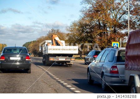 Rear view of multiple vehicles travelling on multi-lane road with autumn trees along roadside under partly cloudy sky day traffic scene transportation journey concept Rear view of multiple vehicles travelling on multi-lane road with autumn trees along roadside under partly cloudy sky day traffic scene transportation journey concept 141438288