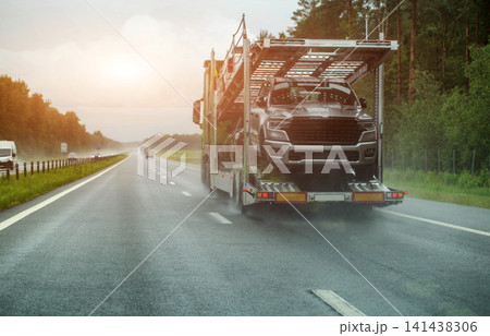Car transporter truck carrying new pickup truck drives on wet highway during heavy rain. Road spray and poor visibility present driving danger. Copy space for text, custom-made car delivery Car transporter truck carrying new pickup truck drives on wet highway during heavy rain. Road spray and poor visibility present driving danger. Copy space for text, custom-made car delivery 141438306