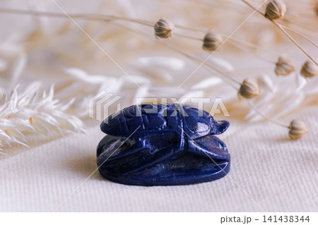Blue stone scarab beetle amulet on linen fabric with dried flowers. Blue stone scarab beetle amulet on linen fabric with dried flowers. 141438344