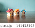 Three colorful miniature toy houses on wooden surface with blue background, real estate and housing market concept 141438392