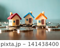 Three colorful miniature toy houses on pile of coins on blue background, real estate investment and mortgage concept 141438400