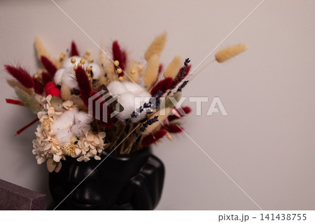 Decorative bouquet of dried flowers and colorful foliage arranged in a glossy black vase against a neutral wall, creating an elegant autumn-inspired home interior accent display Decorative bouquet of dried flowers and colorful foliage arranged in a glossy black vase against a neutral wall, creating an elegant autumn-inspired home interior accent display 141438755