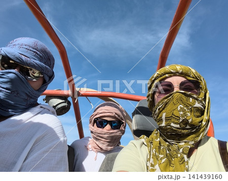 Desert adventure with nomadic travelers three men in traditional headscarves and sunglasses pose on a dune buggy under bright blue sky, capturing the thrill off road exploration in arid landscape. 141439160