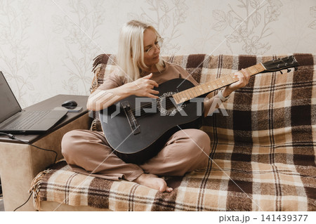 Mature woman learning to play guitar at home Mature woman learning to play guitar at home 141439377