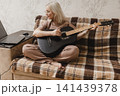 Mature woman practicing guitar beside a laptop at home 141439378