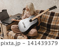 Mature woman using a laptop while holding a guitar at home 141439379