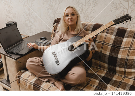 Mature woman with guitar using a laptop at home Mature woman with guitar using a laptop at home 141439380