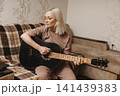Mature woman playing acoustic guitar in her living room 141439383