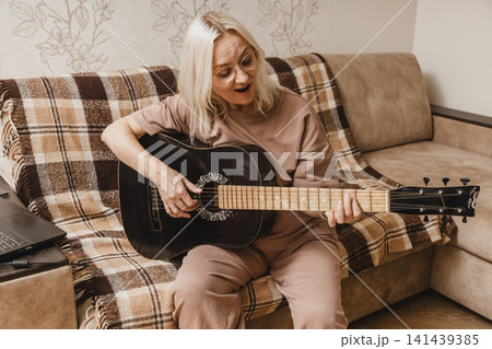 Happy mature woman playing acoustic guitar at home Happy mature woman playing acoustic guitar at home 141439385