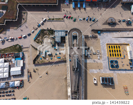 Beautiful top down high altitude aerial panoramic perspective of sea pier entrance sports trampoline park beach clubs colorful cars and promenade boulevard under bright sunlight Beautiful top down high altitude aerial panoramic perspective of sea pier entrance sports trampoline park beach clubs colorful cars and promenade boulevard under bright sunlight 141439822