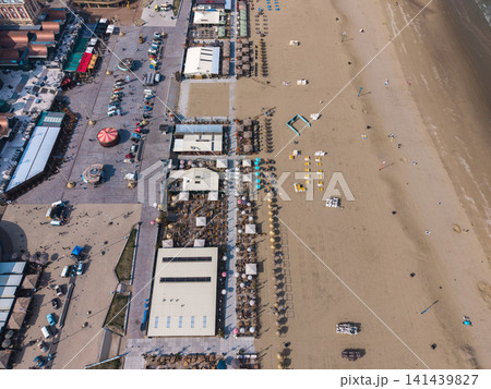 Beautiful high altitude aerial panoramic perspective of beach resort clubs with straw parasols promenade boulevard vintage cars and sandy ocean coast under bright sunlight 141439827