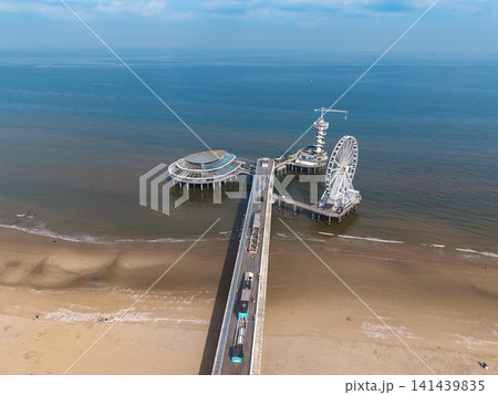 Beautiful high altitude aerial panoramic perspective of iconic sea pier with ferris wheel bungee tower and oval glass pavilion structure extending into the blue ocean water under a clear sky Beautiful high altitude aerial panoramic perspective of iconic sea pier with ferris wheel bungee tower and oval glass pavilion structure extending into the blue ocean water under a clear sky 141439835