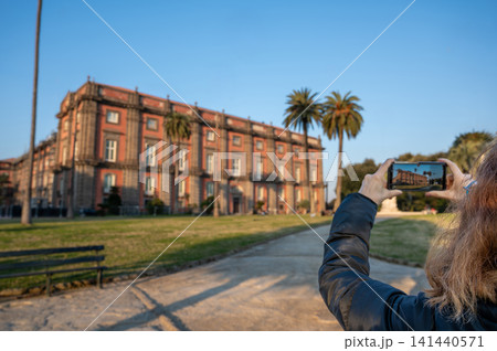 Naples, italy. December 30, 2024. Tourist capturing the historical royal palace of capodimonte, naples, italy, with a smartphone on a sunny day 141440571