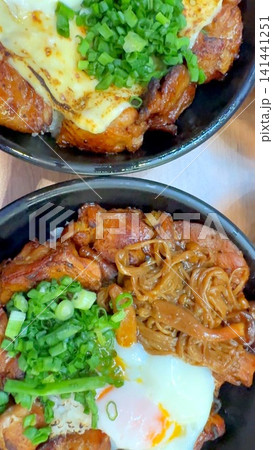 Japanese BBQ rice bowls with grilled chicken, melted cheese, green onions, soft egg, steamed rice, caramelized glaze, and warm savory toppings in closeup overhead view Japanese BBQ rice bowls with grilled chicken, melted cheese, green onions, soft egg, steamed rice, caramelized glaze, and warm savory toppings in closeup overhead view 141441251