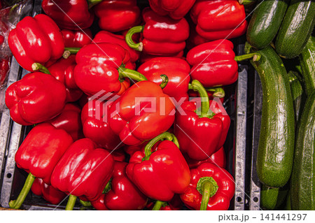 Red bell peppers and zucchinis on grocery store shelf. Fresh paprika and green zucchinis displayed in a produce aisle. Red bell peppers and zucchinis on grocery store shelf. Fresh paprika and green zucchinis displayed in a produce aisle. 141441297