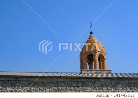 Ancient stone chapel tower with cross, set against blue sky Ancient stone chapel tower with cross, set against blue sky 141442513