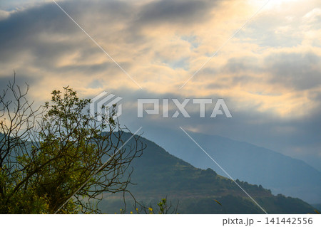 Dramatic sky with golden rays over layered mountain slopes Dramatic sky with golden rays over layered mountain slopes 141442556