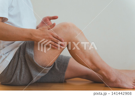 40代男性が床に座って太ももをセルフマッサージするシーン 141442908