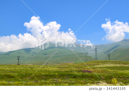 Sunlit mountain meadow with power towers and fluffy clouds 141443195