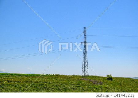 Single electricity transmission tower on grassy hill under bright blue sky Single electricity transmission tower on grassy hill under bright blue sky 141443215
