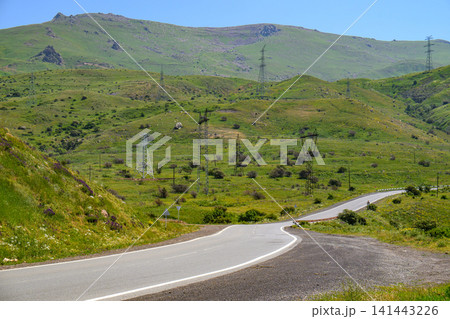 Asphalt road curves through lush green hills under bright blue sky Asphalt road curves through lush green hills under bright blue sky 141443226