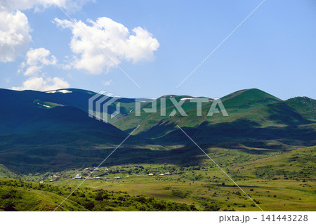 Lush, hilly terrain with green slopes and snowy peaks under a sunny sky Lush, hilly terrain with green slopes and snowy peaks under a sunny sky 141443228