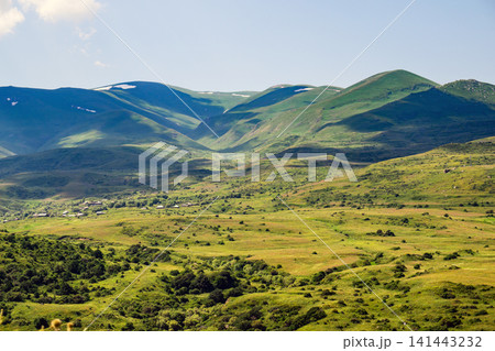 Wide valley framed by lush green mountains with snow-capped peaks 141443232