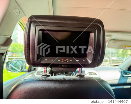 Car headrest screen is installed in the back seat area for entertainment during drive time in a vehicle parked in a city area on a sunny day 141444407