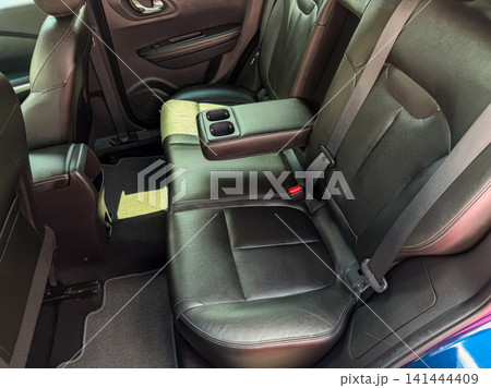 Black leather car seats in the back of a vehicle showing a center console and seat belts in place during daylight 141444409
