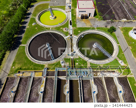 Wastewater treatment facility in operation during daylight hours showcasing multiple treatment tanks filled with different colored water 141444425