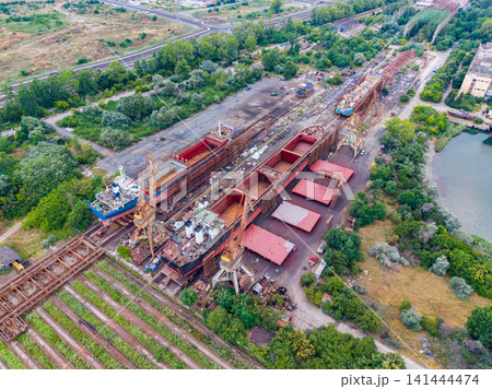 View of a shipyard showing large ships and storage areas with greenery and roads nearby during daytime hours View of a shipyard showing large ships and storage areas with greenery and roads nearby during daytime hours 141444474