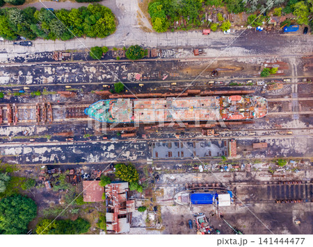 Ship docked at repair yard in a rusted condition with trees and buildings in surrounding area during daylight hours 141444477