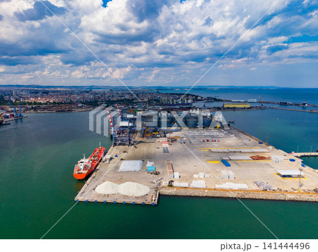 Large cargo terminal at a busy port during the day with clouds above and ocean waters surrounding the area Large cargo terminal at a busy port during the day with clouds above and ocean waters surrounding the area 141444496