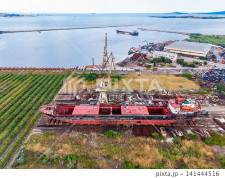 Abandoned shipyard along the water with derelict boats and green fields seen from above in a coastal area Abandoned shipyard along the water with derelict boats and green fields seen from above in a coastal area 141444516