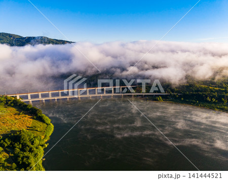 Fog covers a river and bridge in a valley surrounded by mountains in the morning light Fog covers a river and bridge in a valley surrounded by mountains in the morning light 141444521