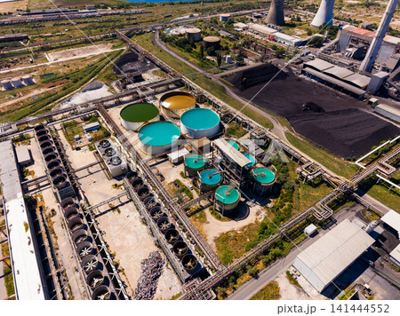 Large industrial site with storage tanks and cooling towers seen from above during the day near a busy city and agricultural land Large industrial site with storage tanks and cooling towers seen from above during the day near a busy city and agricultural land 141444552