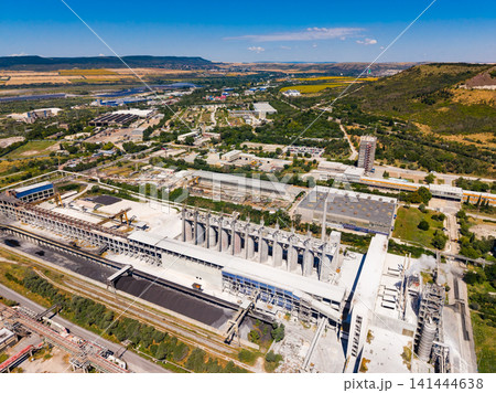 Industrial site seen from above with silos, machinery, and trucks during daytime in a rural area near a river and hills Industrial site seen from above with silos, machinery, and trucks during daytime in a rural area near a river and hills 141444638