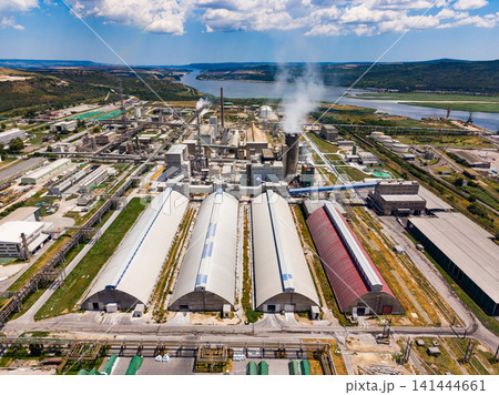 Industrial area shows large buildings and smoke stacks near a river under a bright sky with clouds Industrial area shows large buildings and smoke stacks near a river under a bright sky with clouds 141444661