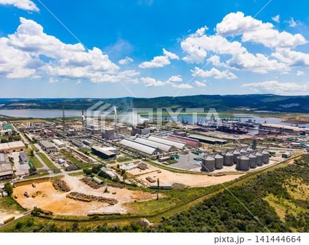 Industrial site with large buildings and silos near a river and hills during a sunny day Industrial site with large buildings and silos near a river and hills during a sunny day 141444664