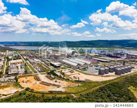 Industrial complex located near river with large buildings and silos under blue sky filled with clouds during daylight Industrial complex located near river with large buildings and silos under blue sky filled with clouds during daylight 141444665