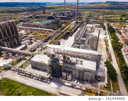 Factory complex located in a rural area with large machines, smokestacks, and storage tanks on a sunny day with blue skies above Factory complex located in a rural area with large machines, smokestacks, and storage tanks on a sunny day with blue skies above 141444669