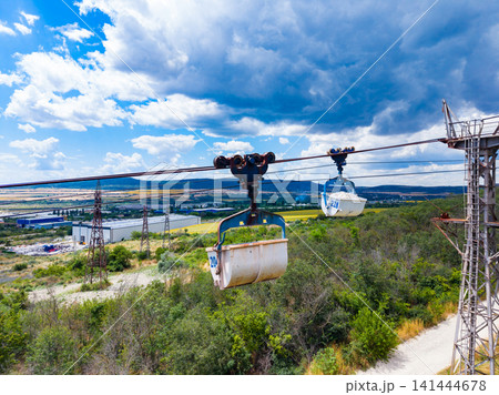 Cable cars travel over fields and hills under a cloudy sky with a view of distant mountains in the background 141444678