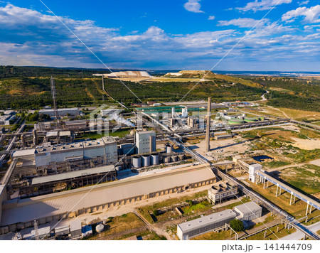 View of an industrial complex with large storage tanks and pipelines located in a rural area under a blue sky with some clouds during the daytime hours View of an industrial complex with large storage tanks and pipelines located in a rural area under a blue sky with some clouds during the daytime hours 141444709