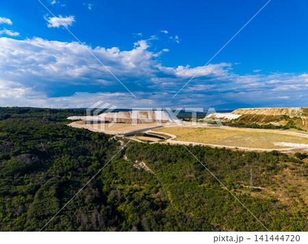 View of a large quarry surrounded by green trees and open land under a blue sky View of a large quarry surrounded by green trees and open land under a blue sky 141444720